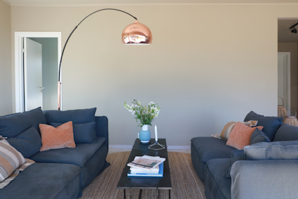 Vardagsrum med mörkblå soffor, ett svart soffbord med blommor och ljusstakar, samt en bågformad golvlampa.