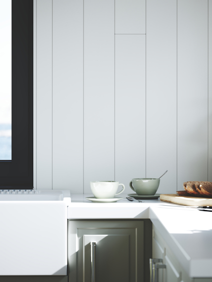 Diskbänk i hörn av kök med vitt skåp, en kopp med fat och sked, och en tallrik bröd vid fönster.