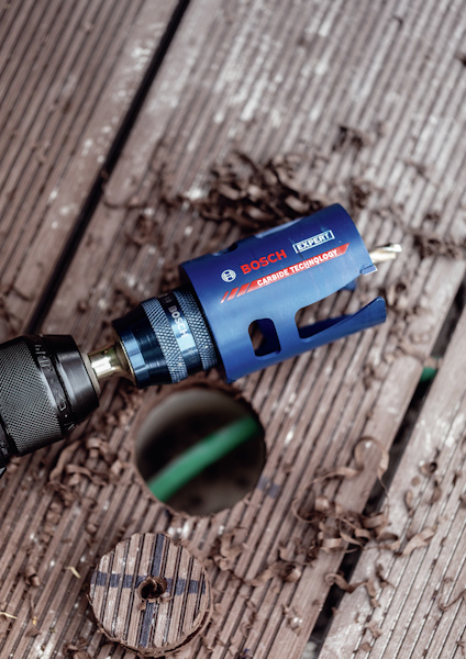 Blå Bosch-hålsåg fäst vid en borrmaskin, omgiven av träspån.