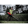 Man in a high-visibility vest using a red trimmer on a hedge, trees and cloudy sky in the background.
