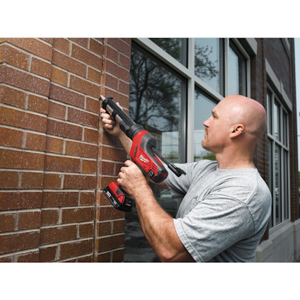 Man applying sealant to brick wall with a cordless caulking gun.