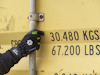 Hand med svarta handskar håller i metallstång framför en gul container med texten "30,480 KGS 67,200 LBS".