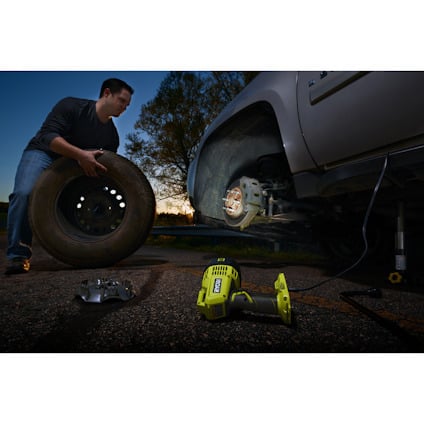 Man vid ett fordon håller i ett stort däck, med en borrmaskin och en strålkastare på marken intill.