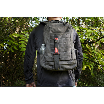 Person med grå ryggsäck står i skog, vattenflaska på sidan.