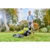 En person klipper gräsmatta med en grön Ryobi gräsklippare i en trädgård med höstfärgade träd.