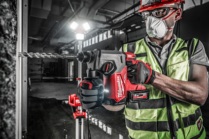 Person i reflexväst och hjälm använder en elektrisk borrmaskin mot en betongvägg.