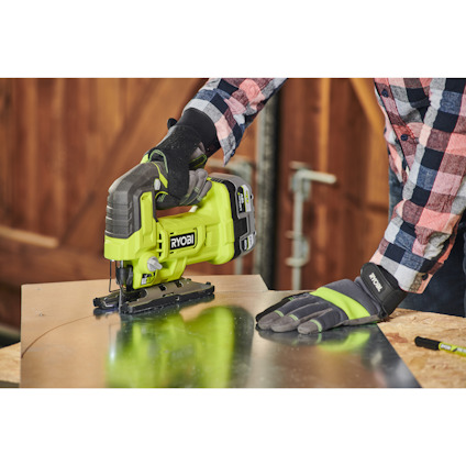 Person använder en grön sticksåg för att skära i en metallplåt.