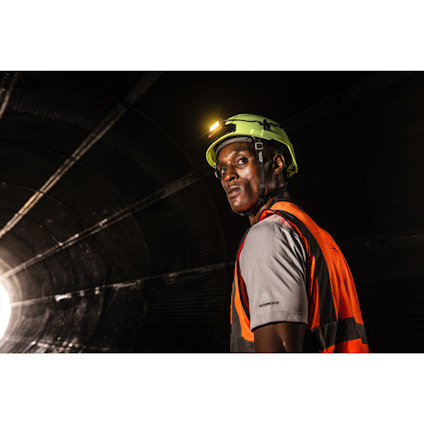Person i hjälm och reflexväst i en upplyst tunnel, med ljus som skiner bakom.