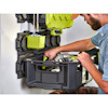 Man in blue shirt organizing tools in a wall-mounted storage system with green containers and a black bin.