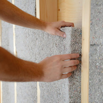 Händer placerar en isoleringsskiva av återvunnet material mellan träreglar.