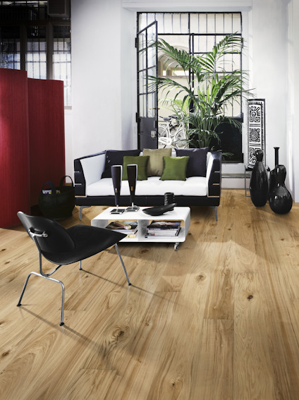 Modernt rum med trägolv, svart och vit inredning, fåtölj, soffbord och växter vid ett stort fönster.