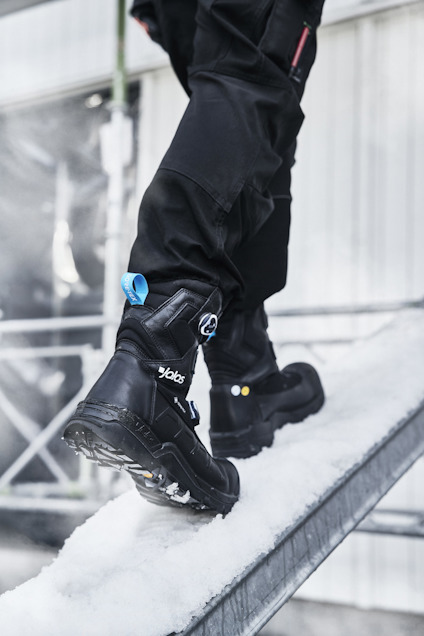 Kängor med halkskyddande sulor kliver på en snötäckt ramp.