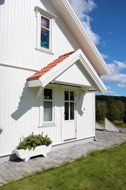 Vitt hus med rött tegeltak, vit dörr med glasrutor, blomsterrabatt framför, grå stengång och gräsmatta.