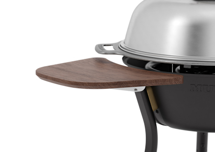 Fällbart sidobord i trä fäst vid en grill med metallkåpa.