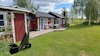Rött trähus med blå dörr, svensk flagga på verandan, gräsmatta och björkar i bakgrunden.
