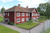 Rött tvåvåningshus med vita fönsterkarmar, omgiven av trädgård; träden i bakgrunden.