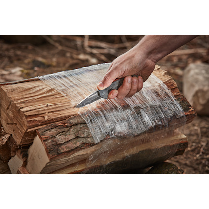 Hand skär plastfolie på vedträ med fickkniv utomhus.