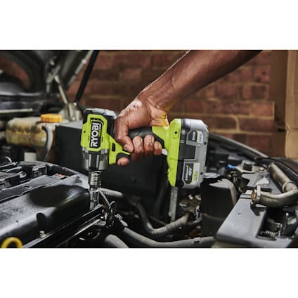 Person använder en grön Ryobi mutterdragare för att arbeta på en bilmotor i ett garage.