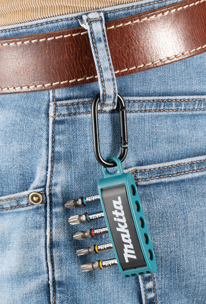 En skruvbitsuppsättning i hållare märkt "Makita" fastsatt på hällan av ett par jeans med karbinhake.
