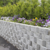 Grå mur av staplade stenar med blommor ovanpå, gröna buskar i bakgrunden.