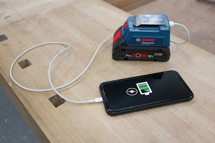 Telefon laddas av Bosch ProCORE 18V batteri via kabel på träbord.
