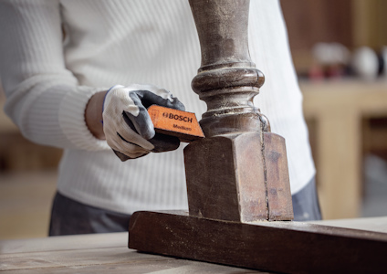 Person slipar träbit med orange slipblock märkt Bosch.