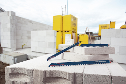 Betongblock staplade på en byggarbetsplats med blå sågblad liggande ovanpå. Gul förvaring i bakgrunden.