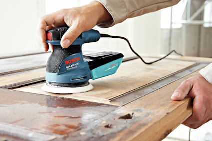 Person slipar trädörr med en blå och svart Bosch excenterslipmaskin.