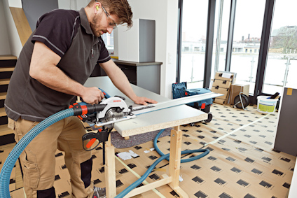 Person hanterar en cirkelsåg på en träbänk i en ljus inomhusmiljö.