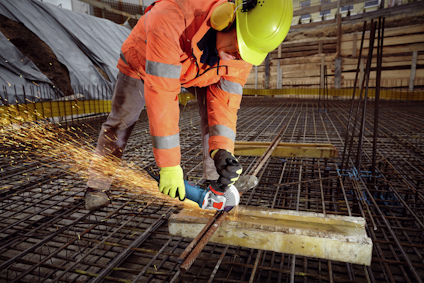 Person som skär armeringsjärn med vinkelslip på byggarbetsplats, gnistor flyger.