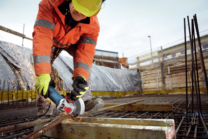 Byggarbetare i säkerhetskläder använder vinkelslip på armeringsjärn vid en byggarbetsplats.