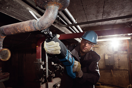 Person i skyddshjälm använder såg för att kapa rör i mörk industrimiljö.