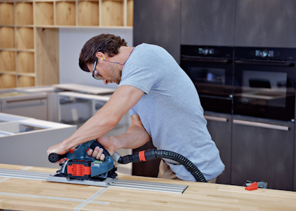 En person använder en cirkelsåg för att såga i en träbräda, med dammsugarslang kopplad till sågen.