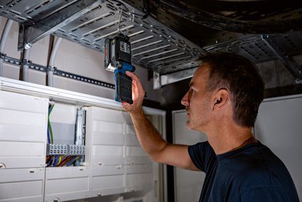 En person använder en digital enhet för att mäta vid ett kabelställ ovanför en elcentral.