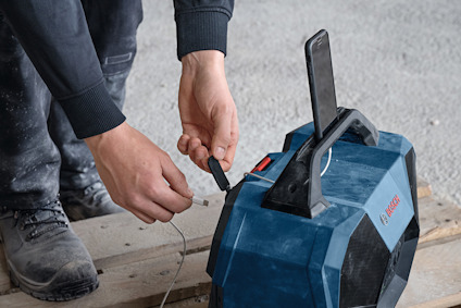 Person som ansluter en kabel till en blå högtalare med handtag, placerad på en träpall.