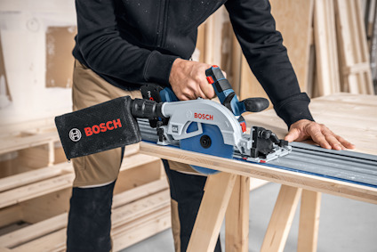 Person använder en Bosch-kapsåg med dammpåse på träbockar i verkstadsmiljö.