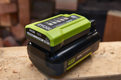 Grön och svart laddare märkt "Ryobi 40V Lithium" på ett bord. Bakgrund med suddiga trästycken.