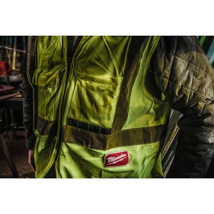 Person wearing a yellow and black high-visibility vest with "Milwaukee" logo, in a workshop setting.
