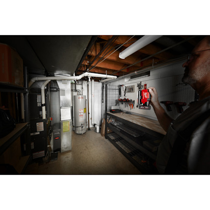 Mörkt rum med en man. Vägg med verktyg och arbetsbänk. Vattenvärmare och ledningar i bakgrunden.