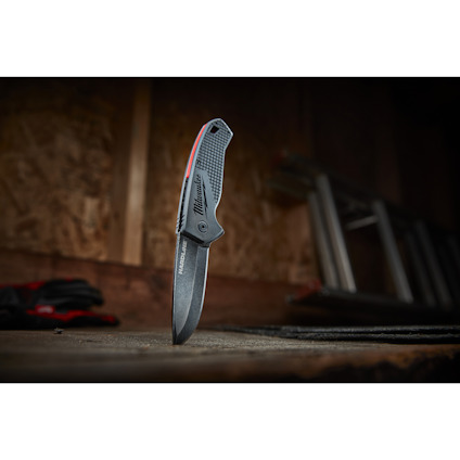 En svartvikskniv står upprätt på ett träbord framför en suddig stege i bakgrunden.