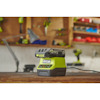 Ryobi batteriladdare och batteri på en arbetsbänk i en verkstad med suddiga verktyg i bakgrunden.