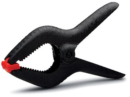 Svart plastklämma med räfflade käftar och rött gummiskydd på spetsarna.