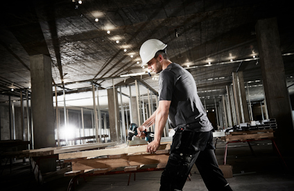 Man i skyddshjälm och skyddsglasögon använder en borrmaskin under byggnation.