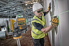 Person med skyddshjälm och väst använder DeWalt-laserverktyg för att markera linjer på en vägg i en industriell miljö.