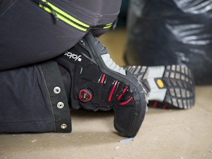 Svart knäskydd med röd detalj på byxor, används av en person som knäböjer.