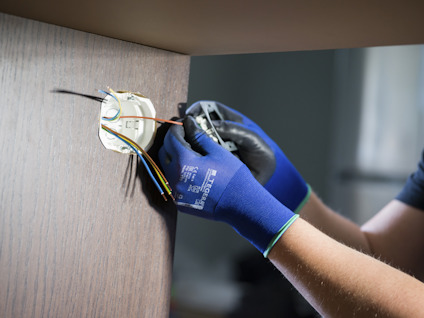 En person med blå handskar installerar eller reparerar elektriska kablar i en väggmonterad enhet.