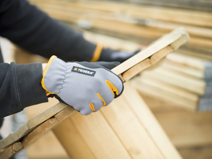 En person bär grå och orange Tegera-arbetshandskar och håller i träplankor.