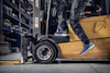 En person i arbetskläder och sneakers sitter på en gul gaffeltruck i ett lager.