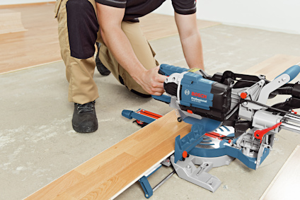 Person använder en kap- och geringssåg för att skära ett träplank på ett golv.