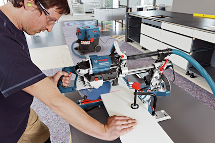 Person arbetar med en skärmaskin för träbearbetning; skyddsglasögon och hörselskydd används.